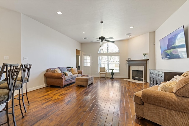 living room featuring baseboards, visible vents, dark wood finished floors, a tile fireplace, and ceiling fan