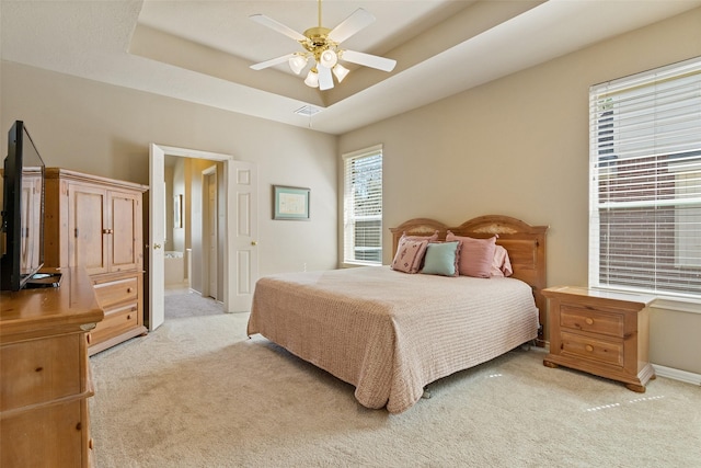 bedroom featuring light carpet, a raised ceiling, ensuite bathroom, a ceiling fan, and baseboards