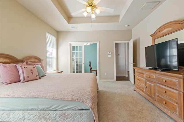 bedroom with a raised ceiling, baseboards, visible vents, and light carpet