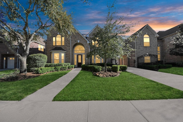 view of front of property with brick siding, a lawn, and a gate