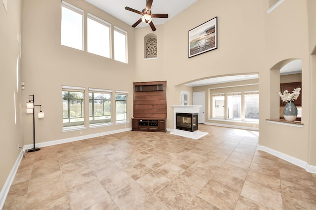 unfurnished living room featuring a multi sided fireplace, baseboards, plenty of natural light, and ceiling fan