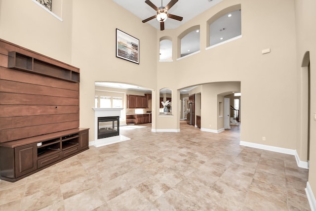 unfurnished living room with a ceiling fan, arched walkways, a multi sided fireplace, and baseboards