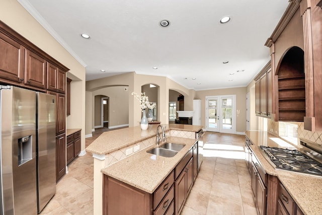 kitchen with a kitchen island with sink, arched walkways, a sink, stainless steel appliances, and open floor plan