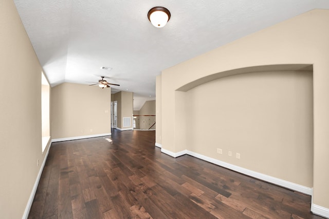 spare room with visible vents, baseboards, ceiling fan, vaulted ceiling, and dark wood-style floors