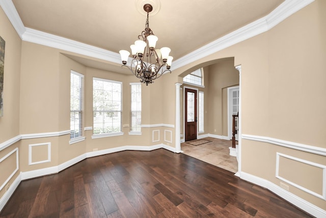 unfurnished dining area featuring crown molding, baseboards, dark wood-type flooring, an inviting chandelier, and arched walkways