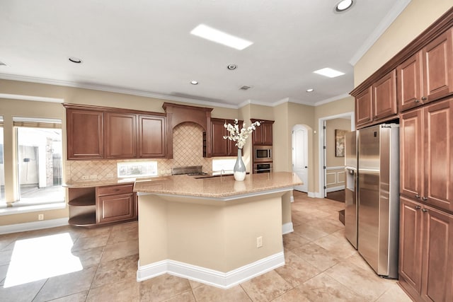 kitchen featuring tasteful backsplash, an island with sink, ornamental molding, arched walkways, and stainless steel appliances