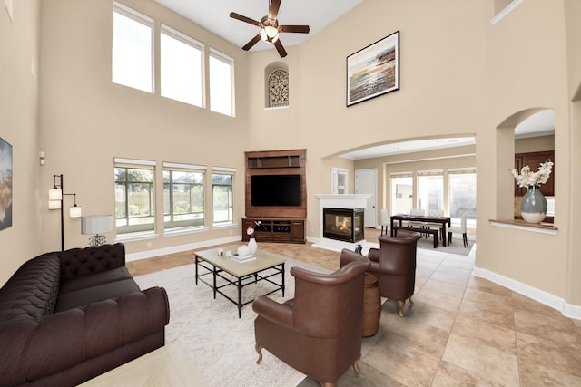 living room featuring baseboards, arched walkways, a glass covered fireplace, and a ceiling fan