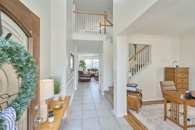 entrance foyer featuring a high ceiling, light tile patterned flooring, crown molding, baseboards, and stairs