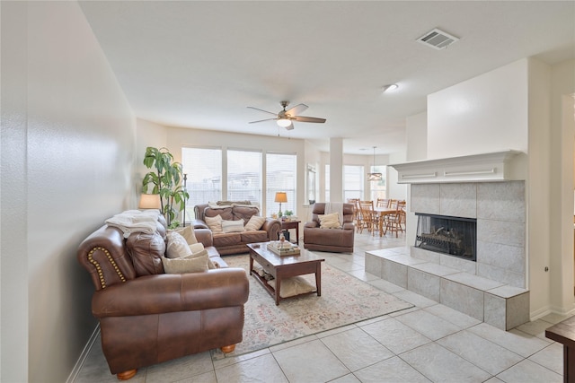 living room featuring visible vents, a tiled fireplace, light tile patterned floors, baseboards, and ceiling fan