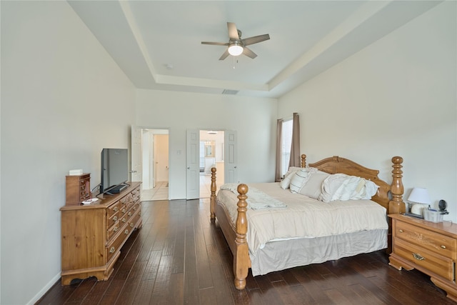 bedroom featuring a tray ceiling, visible vents, dark wood-style flooring, and baseboards