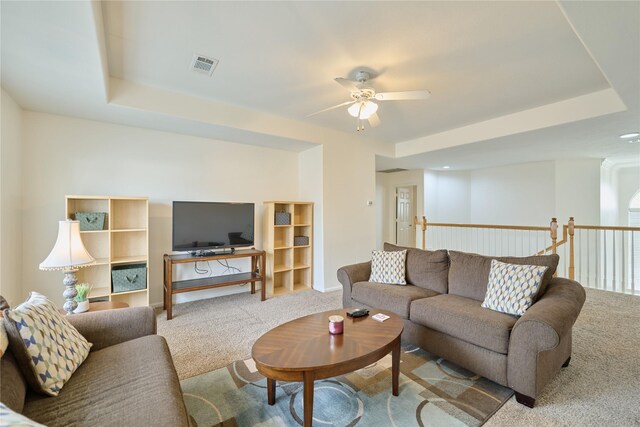 living room with a tray ceiling, carpet flooring, visible vents, and ceiling fan