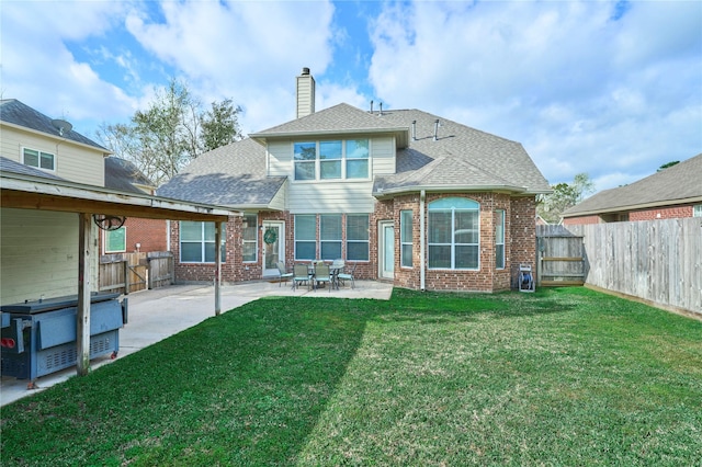 rear view of house with a patio area, brick siding, a fenced backyard, and a shingled roof