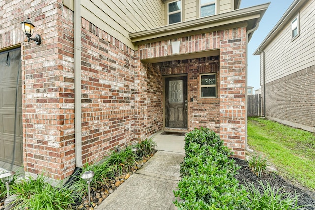 view of exterior entry featuring brick siding, a garage, and fence