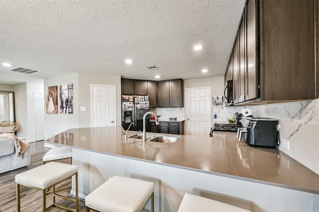 kitchen with a peninsula, a sink, dark brown cabinets, stainless steel refrigerator with ice dispenser, and black microwave