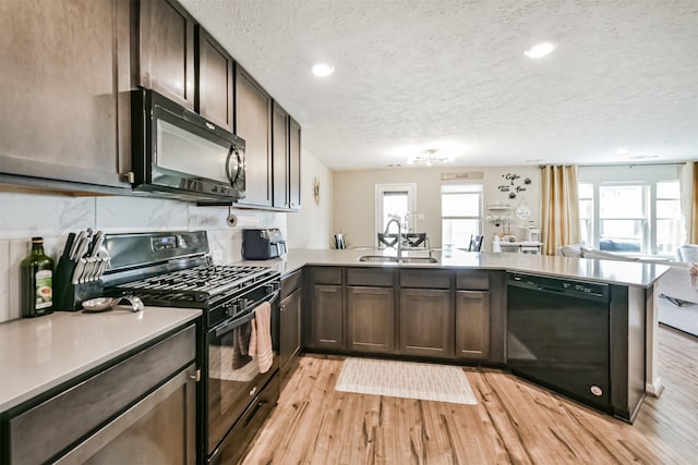 kitchen with light countertops, a peninsula, light wood-style floors, black appliances, and a sink