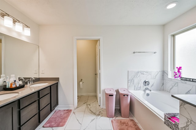 full bath featuring baseboards, a garden tub, double vanity, marble finish floor, and a sink