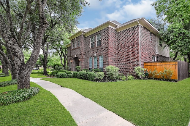 view of side of property featuring a yard, fence, and brick siding