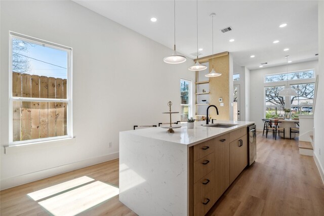 kitchen with visible vents, a sink, dishwasher, light wood-type flooring, and a kitchen island with sink