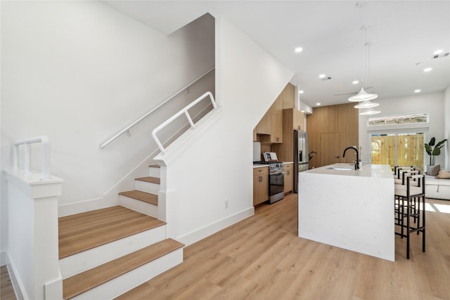 kitchen featuring light countertops, appliances with stainless steel finishes, light wood-style floors, modern cabinets, and a kitchen island with sink