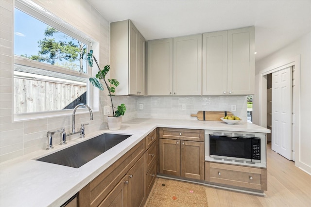 kitchen featuring stainless steel microwave, backsplash, light countertops, and a sink