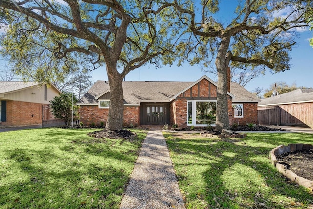 view of front facade featuring brick siding, roof with shingles, a front yard, and fence