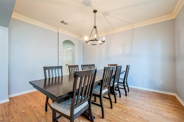 dining space with arched walkways, light wood-style flooring, an inviting chandelier, and ornamental molding