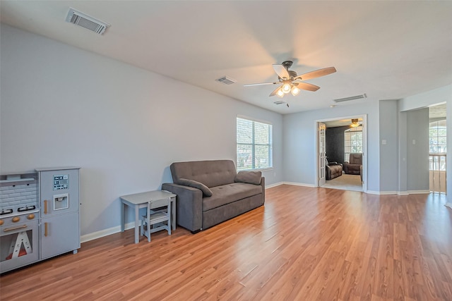 living area featuring light wood-style floors, a ceiling fan, and visible vents