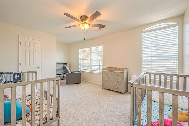 carpeted bedroom with baseboards, visible vents, a crib, and a ceiling fan