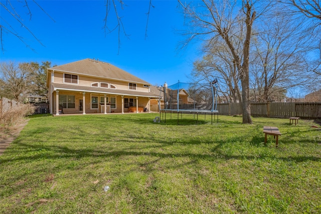 rear view of house with a yard, a trampoline, and fence