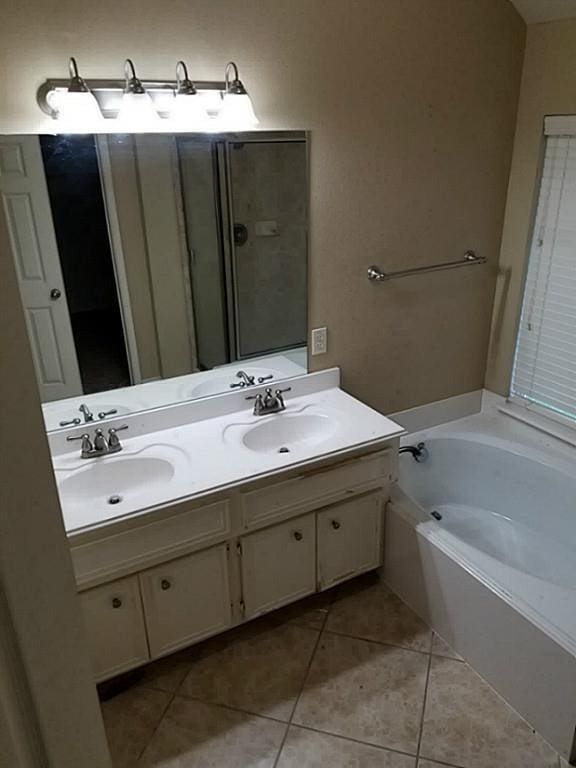 full bath featuring tile patterned floors, a garden tub, double vanity, and a sink