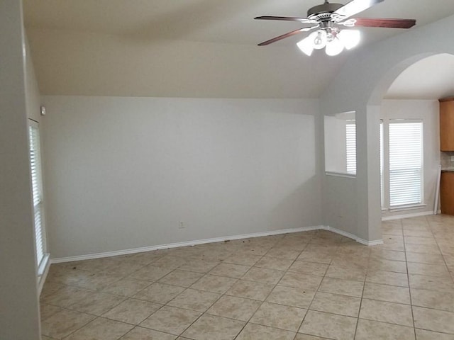 empty room featuring arched walkways, light tile patterned flooring, baseboards, ceiling fan, and vaulted ceiling