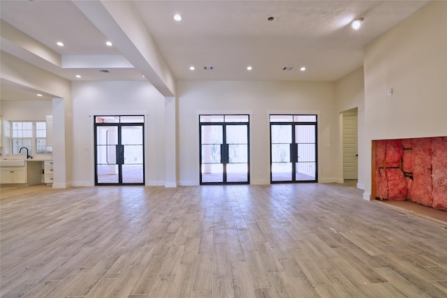 interior space featuring a healthy amount of sunlight, french doors, light wood-style floors, and a towering ceiling