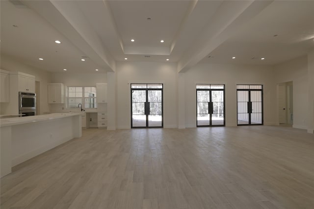 unfurnished living room with a high ceiling, recessed lighting, light wood-style floors, and a sink