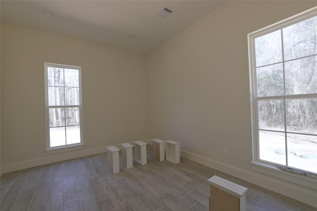 spare room with wood finished floors, visible vents, and baseboards