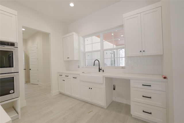 kitchen with white cabinetry, double oven, light wood-style flooring, and a sink