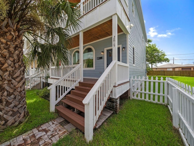 doorway to property featuring a lawn, a porch, and fence