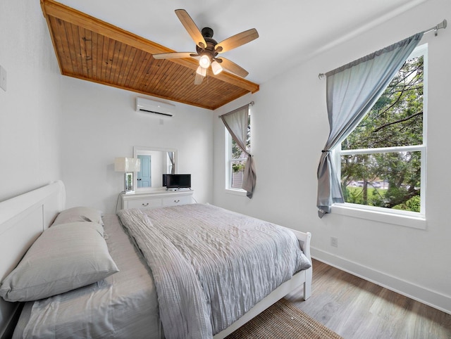 bedroom featuring multiple windows, an AC wall unit, baseboards, and wood finished floors