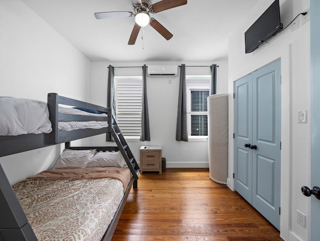 bedroom featuring a wall mounted air conditioner, baseboards, wood finished floors, and ceiling fan