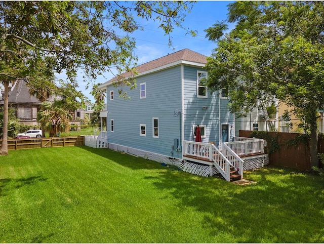 rear view of house featuring a wooden deck, a yard, and fence