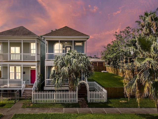 view of front of home with a fenced front yard, stairway, covered porch, a balcony, and a yard