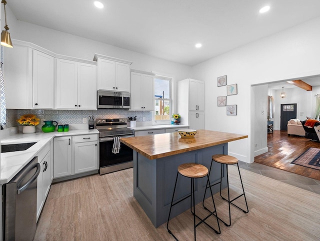 kitchen featuring a kitchen bar, wood counters, tasteful backsplash, appliances with stainless steel finishes, and white cabinets