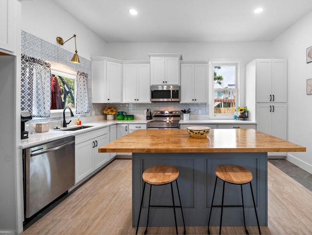 kitchen featuring a breakfast bar, a sink, white cabinetry, stainless steel appliances, and butcher block counters