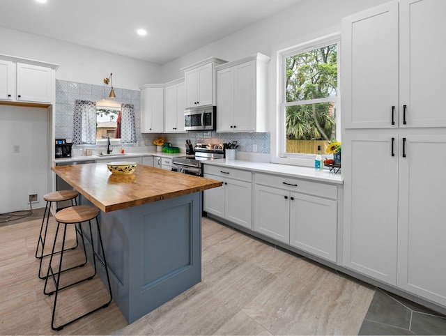 kitchen with a sink, wood counters, appliances with stainless steel finishes, white cabinets, and decorative backsplash