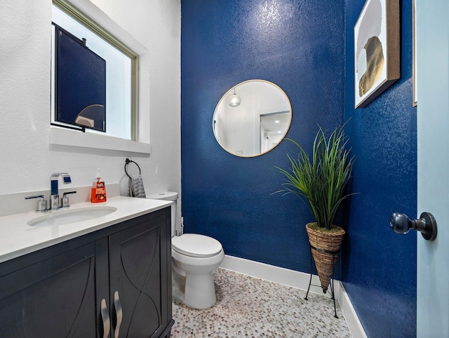 bathroom with baseboards, toilet, vanity, and a textured wall