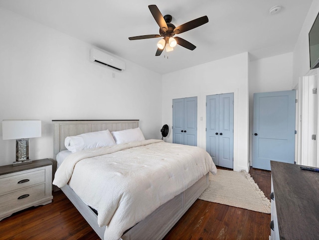 bedroom with an AC wall unit, a ceiling fan, dark wood-style flooring, and two closets