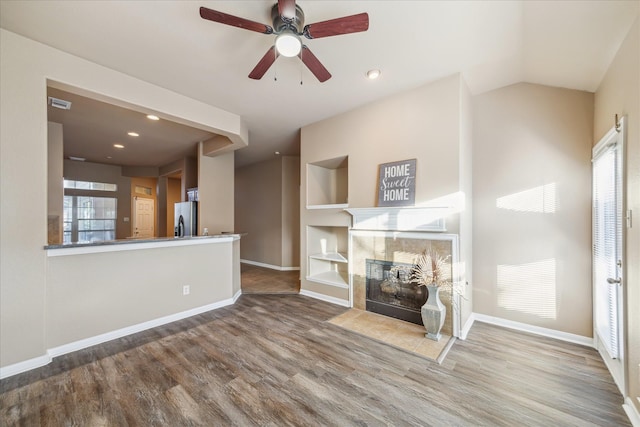 unfurnished living room featuring baseboards, wood finished floors, a ceiling fan, and a tile fireplace