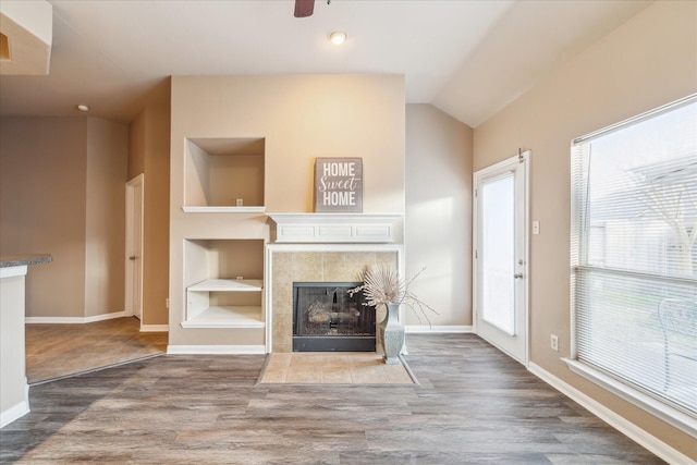 unfurnished living room featuring built in shelves, lofted ceiling, baseboards, and wood finished floors