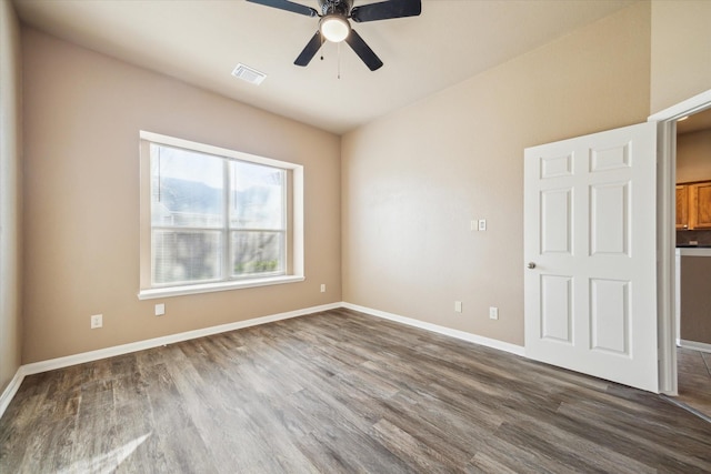 spare room with a ceiling fan, dark wood-style floors, visible vents, and baseboards