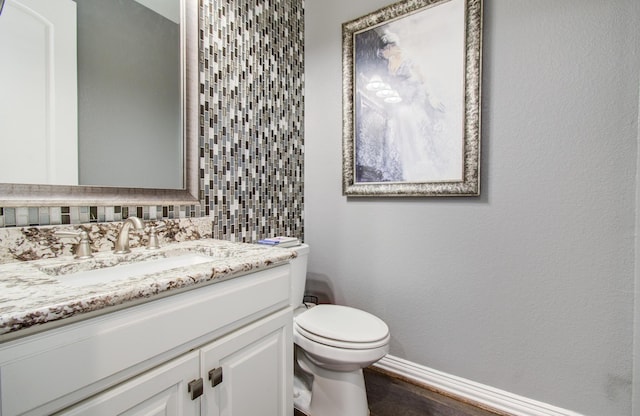 bathroom featuring toilet, backsplash, wood finished floors, baseboards, and vanity