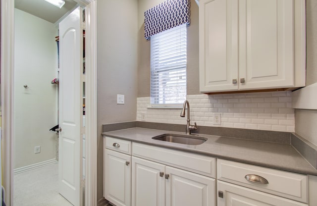 kitchen with dark countertops, decorative backsplash, white cabinets, and a sink